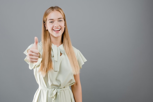 Bella ragazza bionda sorridente che mostra i pollici in su isolati