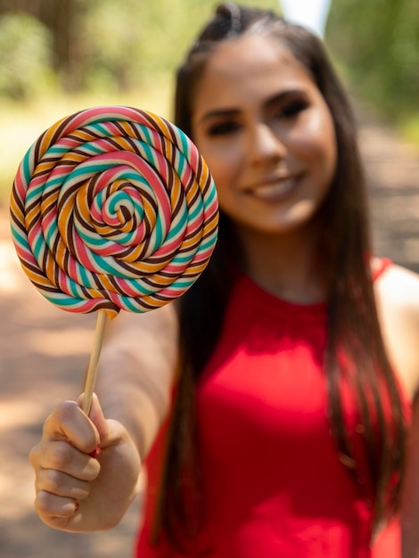 Bella ragazza bruna che tiene lecca-lecca colorato nella foresta Messa a fuoco selettiva