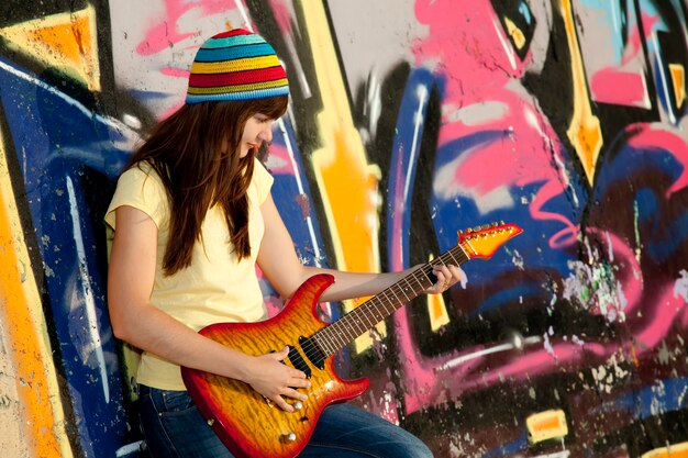 Bella ragazza bruna con chitarra e muro di graffiti