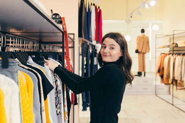 Bella ragazza bruna, con i capelli ricci, sceglie i vestiti in una boutique