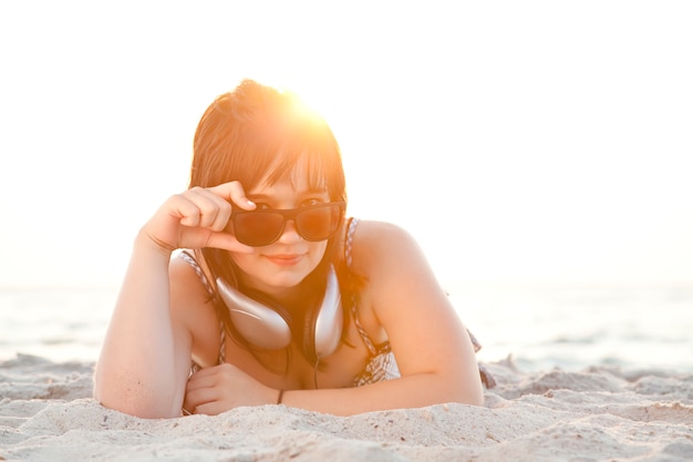 Bella ragazza bruna con le cuffie in spiaggia di sabbia.