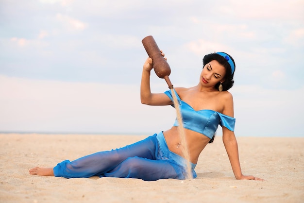 Bella ragazza bruna in costume di danza del ventre seduta sulla sabbia al tramonto