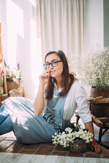 Bella ragazza bruna in un grembiule tra il negozio di fiori. Concetto di primavera, mazzi di fiori freschi.