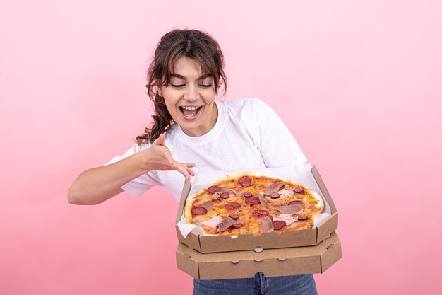 Bella ragazza bruna sorridente, con in mano una scatola di pizza per la consegna, sfondo rosa, copia spazio.