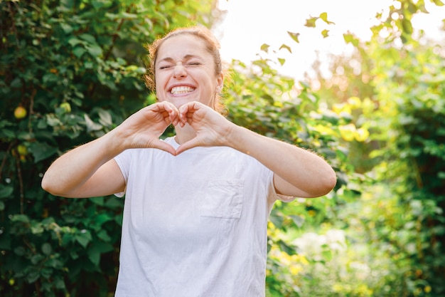 Bella ragazza brunete che mostra il segno del cuore con le mani su sfondo verde parco o giardino