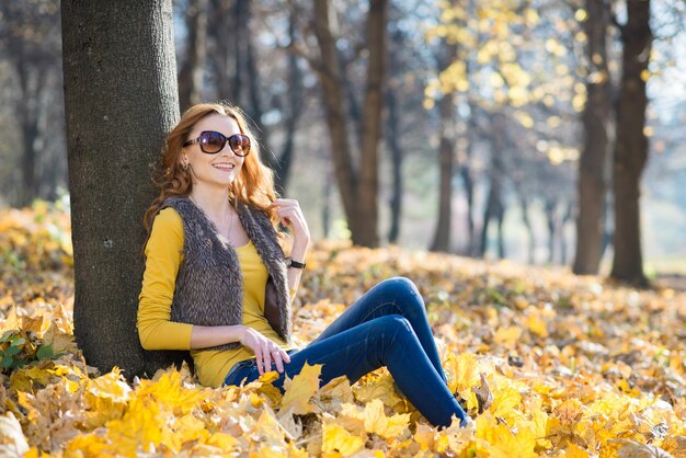 Bella ragazza cammina nel parco autunnale con foglie cadute gialle