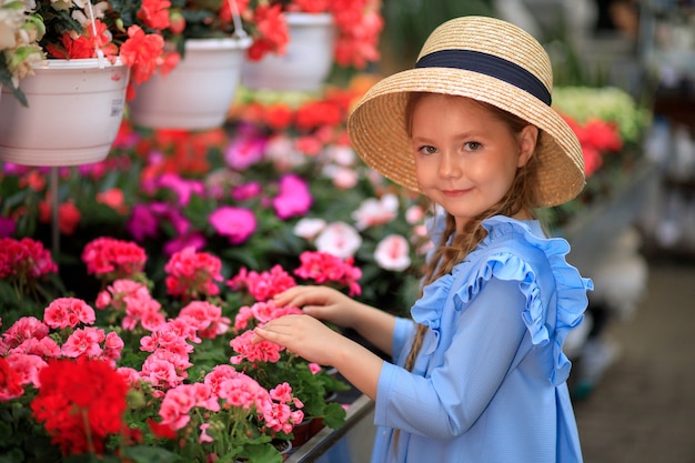 Bella ragazza carina con un cappello di paglia in una serra con fiori colorati