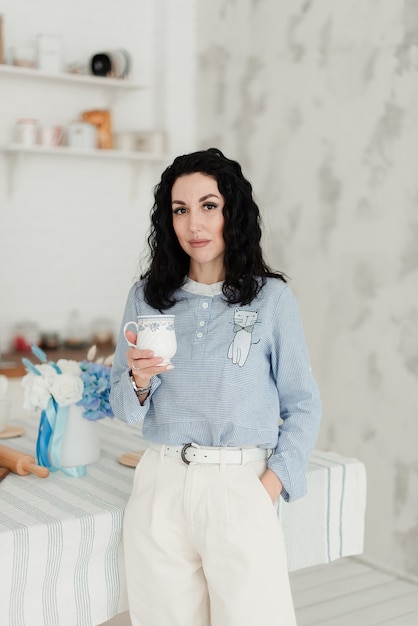 Bella ragazza castana con capelli ondulati neri che tiene una tazza nelle sue mani