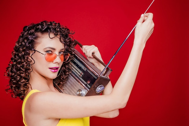 Bella ragazza castana con l'acconciatura riccia in posa con una radio retrò