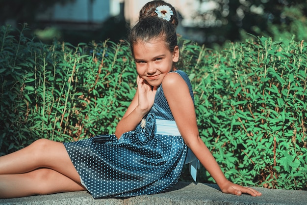 Bella ragazza castana in un vestito blu a pois in estate nel parco. Bambino alla moda in natura. Foto di alta qualità