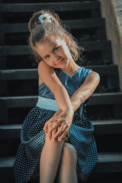 Bella ragazza castana in un vestito blu a pois sui gradini delle scale nel parco. Foto di alta qualità