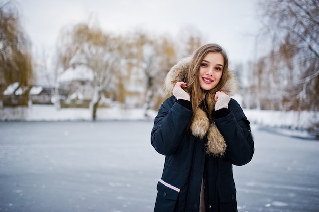 Bella ragazza castana in vestiti caldi di inverno. Modello su giacca invernale contro il lago ghiacciato al parco.