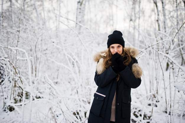 Bella ragazza castana in vestiti caldi di inverno. Modello su giacca invernale e cappello nero.