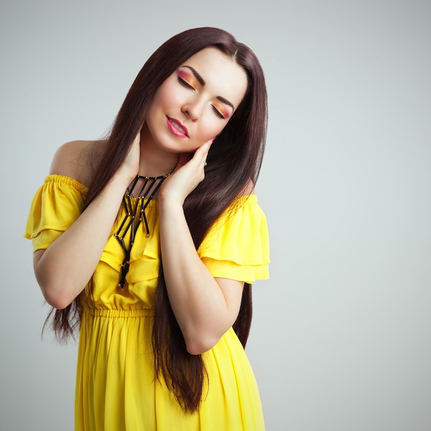 Bella ragazza castana romantica con capelli lunghi in vestito giallo che posa nello studio