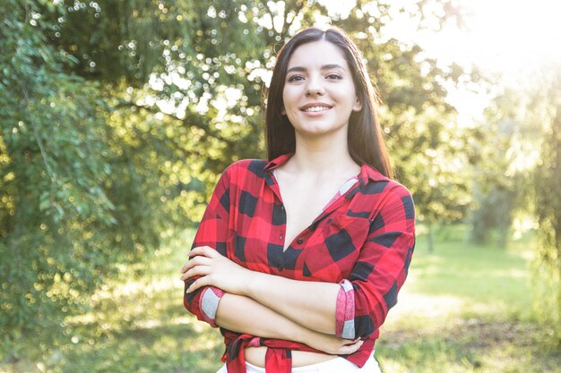 Bella ragazza castana sorridente in una camicia di plaid rossa con le armi attraversate