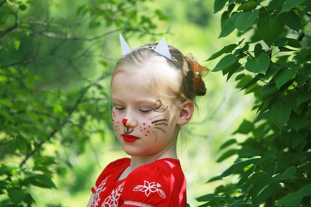 Bella ragazza caucasica bionda sorridente felice con la faccia dipinta come un gatto sullo sfondo della natura estiva