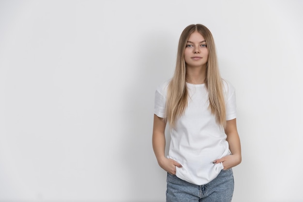 Bella ragazza caucasica si erge su uno sfondo bianco e guarda la telecamera