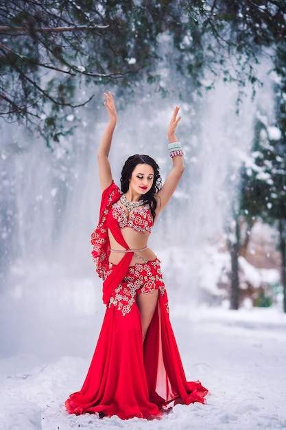Bella ragazza che balla la danza del ventre in vestito rosso in inverno in un parco sulla neve.