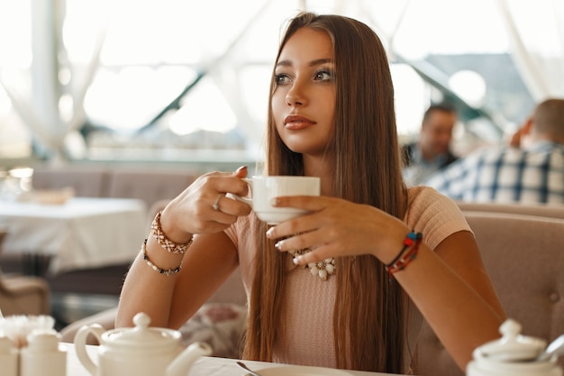 Bella ragazza che beve il tè in un caffè estivo