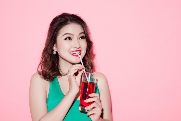 Bella ragazza che beve un cocktail su sfondo rosa