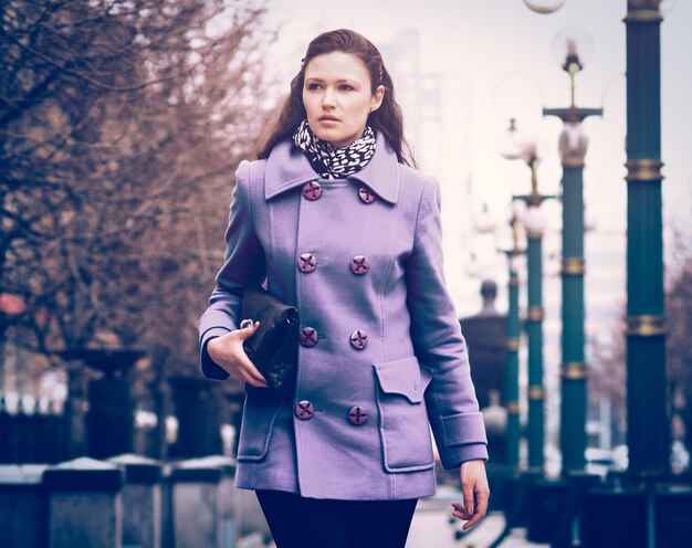 Bella ragazza che cammina per strada con il cappotto trasparente fialetovom all'ora del giorno, e pensava distogliere lo sguardo