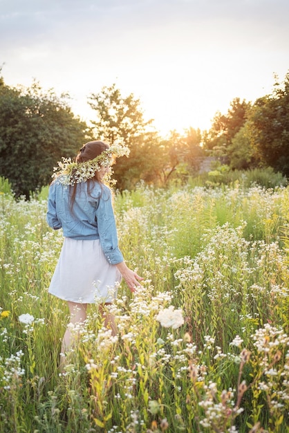 Bella ragazza che cammina sul campo in estate con fiori di campo