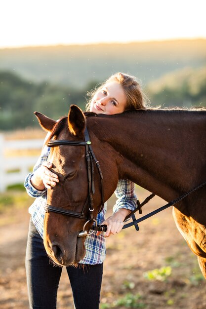 Bella ragazza che conduce il suo cavallo marrone alla fattoria