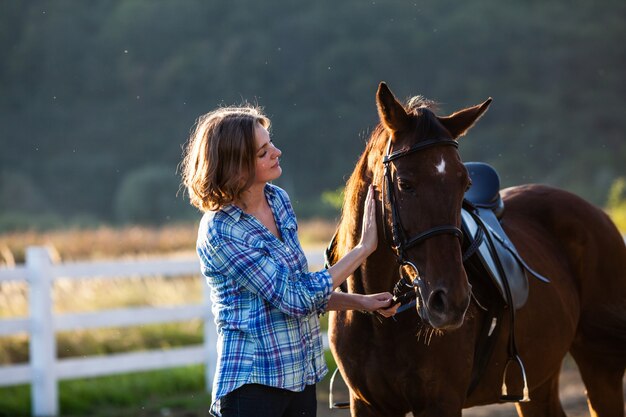 Bella ragazza che conduce il suo cavallo marrone alla fattoria