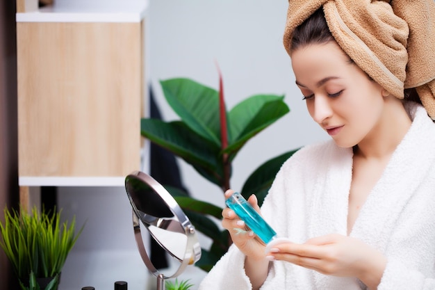 Bella ragazza che fa le procedure cosmetiche a casa davanti allo specchio.