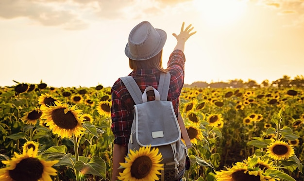 Bella ragazza che gode della natura sul campo dei girasoli al tramonto