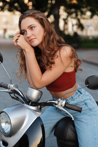 Bella ragazza che indossa abbigliamento estivo casual seduto su uno scooter all'aperto per le strade della città