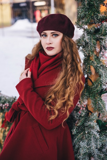 Bella ragazza che indossa un cappotto rosso e un berretto sulla strada di Natale