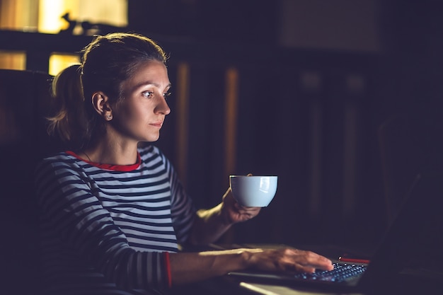 Bella ragazza che lavora di notte su un laptop, all'aperto.