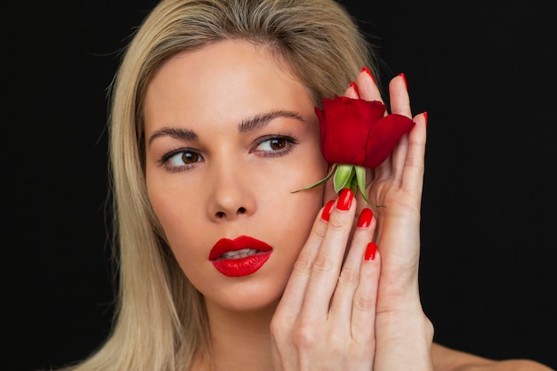 Bella ragazza che posa con una rosa rossa su un'oscurità