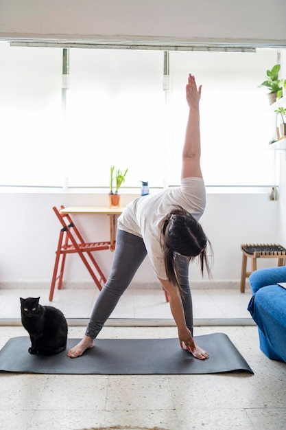 bella ragazza che pratica esercizio e yoga nel suo soggiorno con un gatto nero