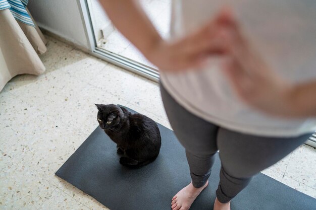 bella ragazza che pratica esercizio nel soggiorno di casa sua con il suo gatto nero