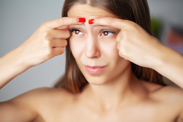 Bella ragazza che schiaccia i brufoli nello specchio del bagno.