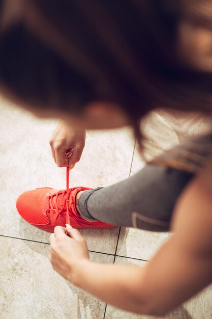 Bella ragazza che si prepara per l'allenamento in palestra. Sta legando i lacci delle scarpe alle scarpe da ginnastica. Vista dall'alto.