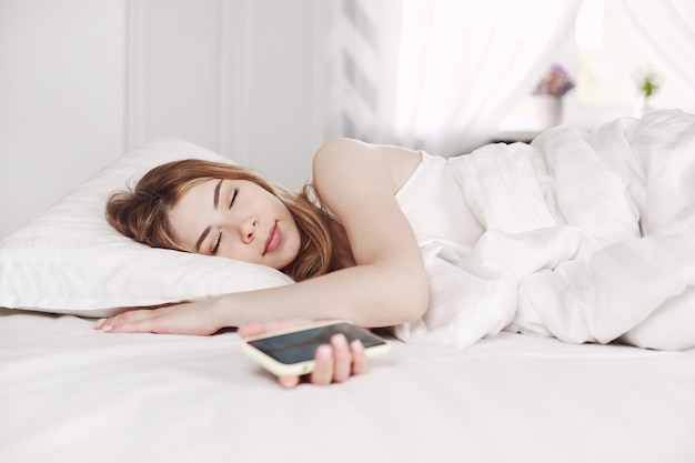 Bella ragazza che si rilassa a letto con il suo smartphone