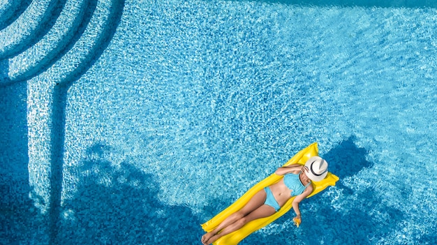 Bella ragazza che si rilassa in piscina, nuota sul materasso gonfiabile e si diverte in acqua in vacanza con la famiglia, località di villeggiatura tropicale, vista aerea del drone dall'alto