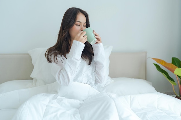 Bella ragazza che si siede e che beve tè caldo al mattino