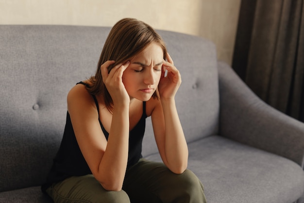 Bella ragazza che soffre di mal di testa, tenendo le mani sulle tempie, chiudendo gli occhi a causa del dolore.