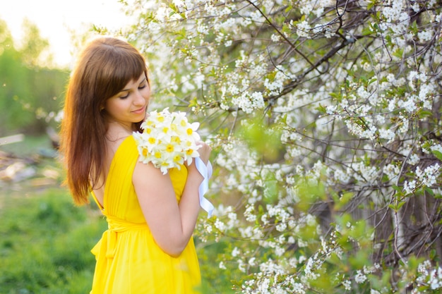 Bella ragazza che sorride con un mazzo dei fiori all'aperto in primavera