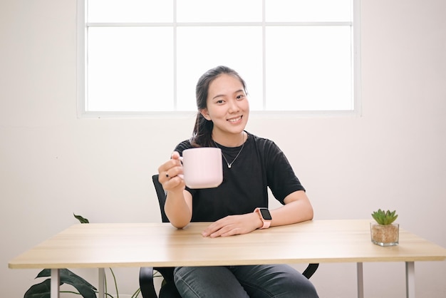 Bella ragazza che sorride e mostra la tazza rosa a casa