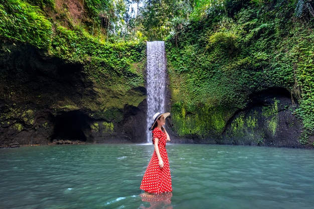 Bella ragazza che sta in cascata di Tibumana in Bali, Indonesia.