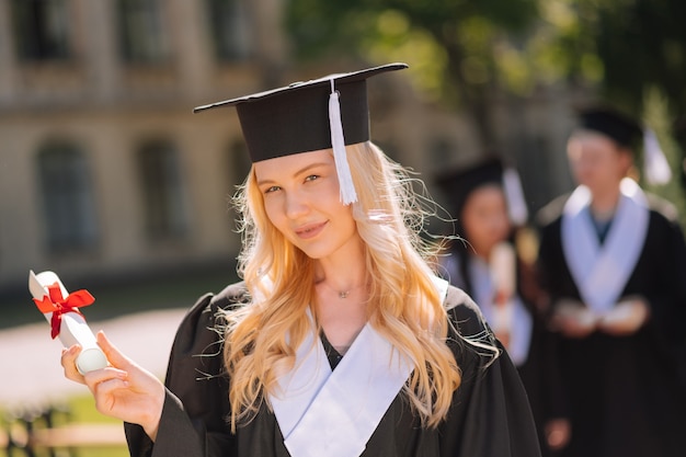 Bella ragazza che tiene il suo diploma arrotolato con il nastro rosso