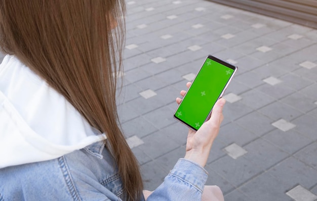 Bella ragazza che tiene uno smartphone nelle mani di uno schermo verde schermo verde