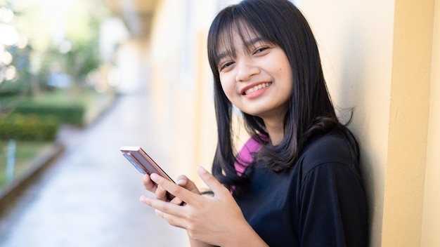 Bella ragazza che usa lo smartphone a scuolaRagazza asiatica Sfondo arancione