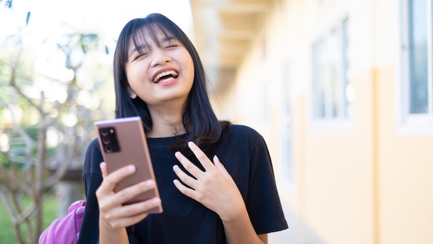 Bella ragazza che utilizza smart phone a scuola, ragazza asiatica, sfondo arancione.