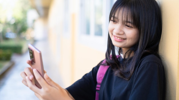 Bella ragazza che utilizza smart phone a scuola, ragazza asiatica, sfondo arancione.